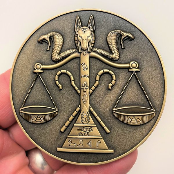 Load image into Gallery viewer, Gold metal coin in hand showing jackal head and cobras on top of scale with Egyptian symbols on it
