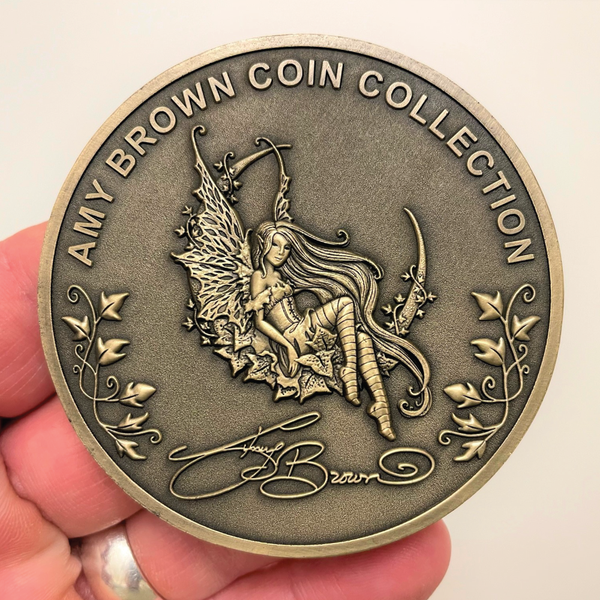 Load image into Gallery viewer, Gold metal coin in hand showing fairy, leaves, and words Amy Brown Coin Collection