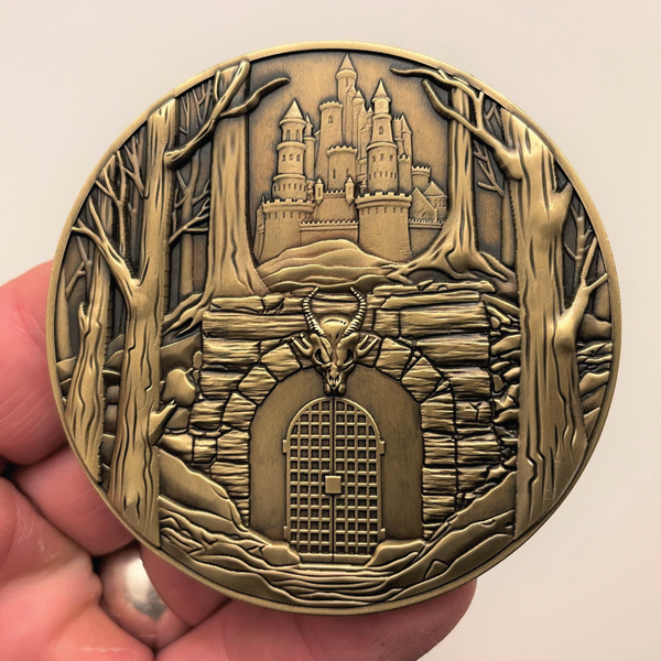 Load image into Gallery viewer, Gold metal coin in hand showing gated dungeon entrance below castle