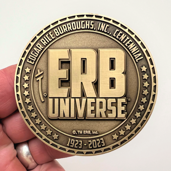 Load image into Gallery viewer, Gold metal coin in hand showing ERB Universe logo