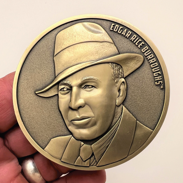 Load image into Gallery viewer, Gold metal coin in hand showing portrait of Edgar Rice Burroughs