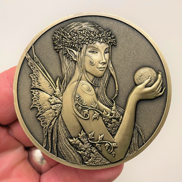 Load image into Gallery viewer, Gold metal coin in hand showing fairy with ball in fairy hand