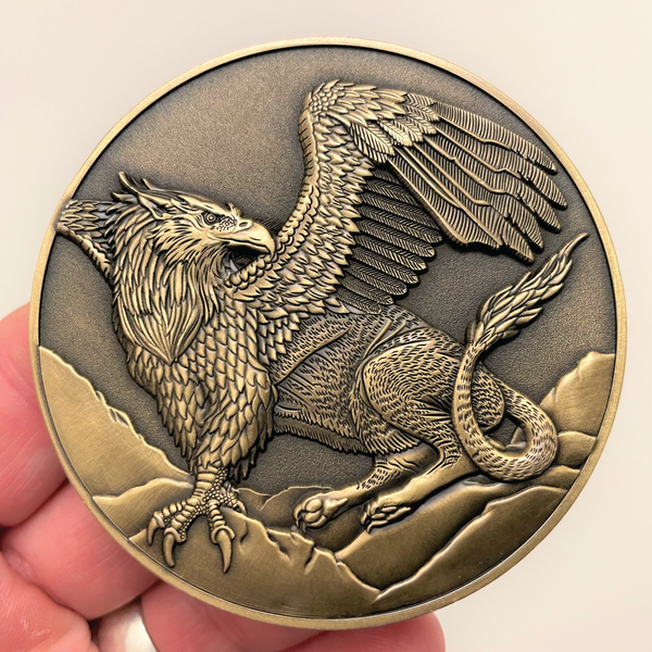 Load image into Gallery viewer, Gold metal coin in hand showing Griffon