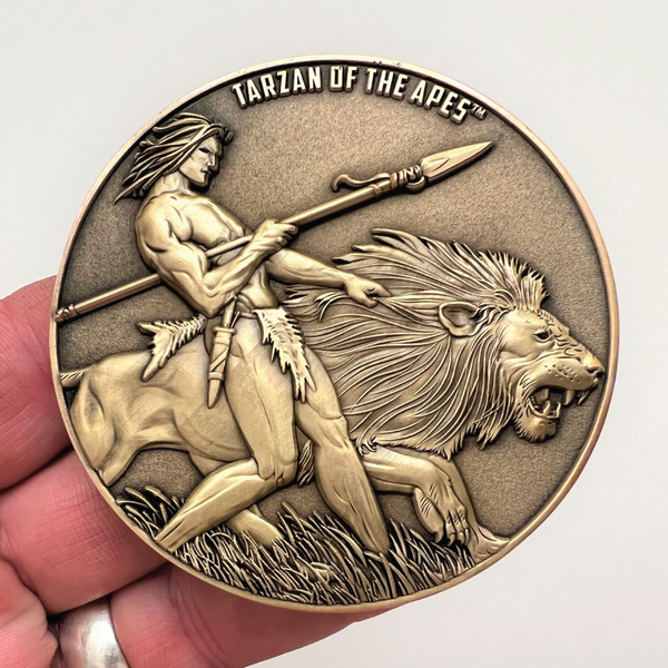 Load image into Gallery viewer, Gold metal coin in hand showing Tarzan of the Apes
