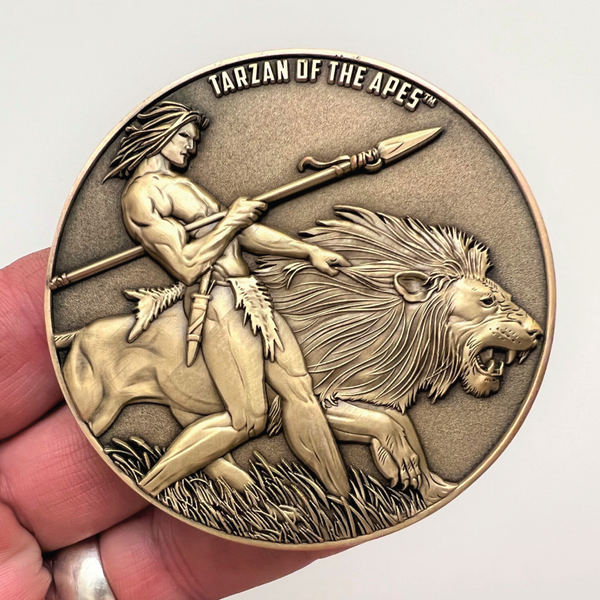 Load image into Gallery viewer, Gold metal coin in hand showing Tarzan of the Apes