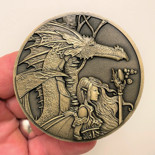 Load image into Gallery viewer, Gold metal coin in hand showing fairy and dragon next to her