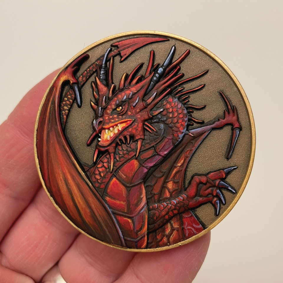 Gold metal coin, features a dragon, that is painted red with black highlights