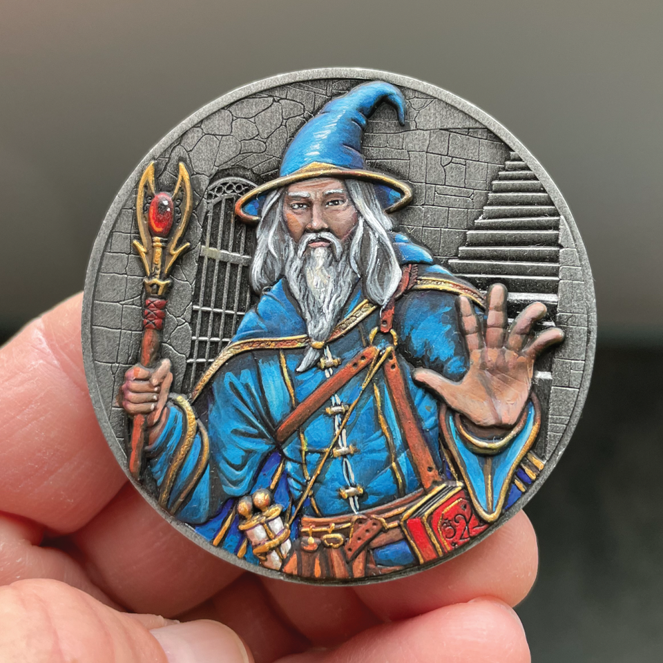 Silver metal coin showing a Wizard with staff.  Wizard clothing is blue with brown highlights.  Wizard has a white beard