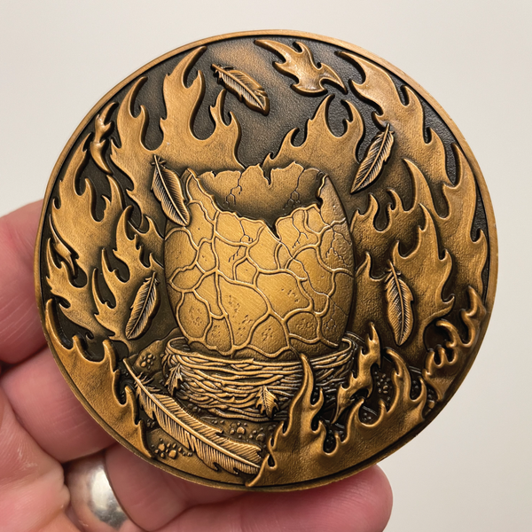 Load image into Gallery viewer, Copper metal coin in hand showing egg surrounded by fire
