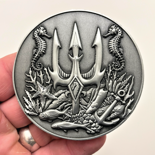 Load image into Gallery viewer, Silver metal coin in hand showing trident, seahorses, and fish
