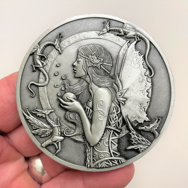 Load image into Gallery viewer, Silver metal coin in hand showing fairy and small dragons around her
