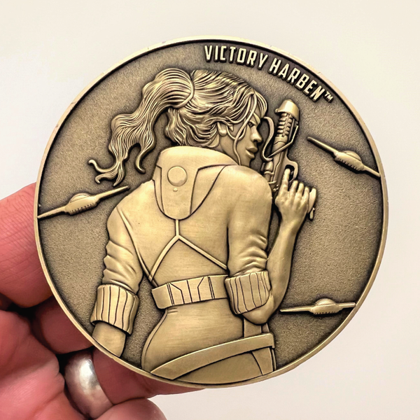 Load image into Gallery viewer, Gold metal coin in hand showing Victory Harben
